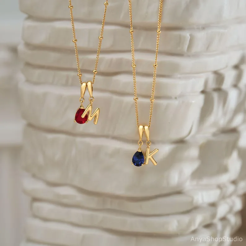 Two gold initial necklaces with ruby and sapphire birthstones